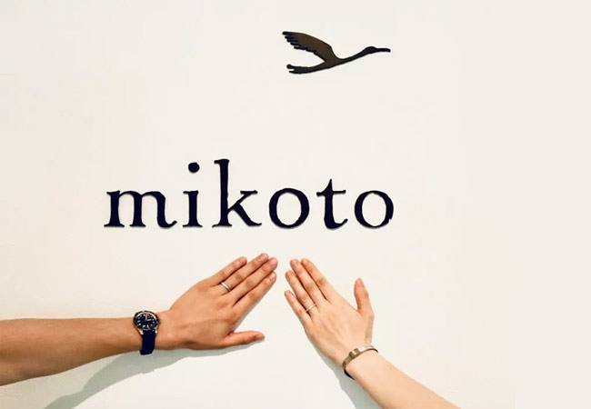 オーダーメイドの結婚指輪を付けたお客様の手と鶴(mikoto)のブランドロゴ